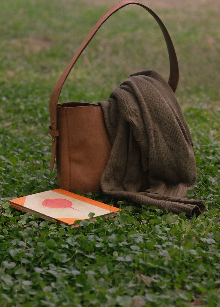 A brown leather bag and notebook on green grass, evoking a natural and cozy setting.