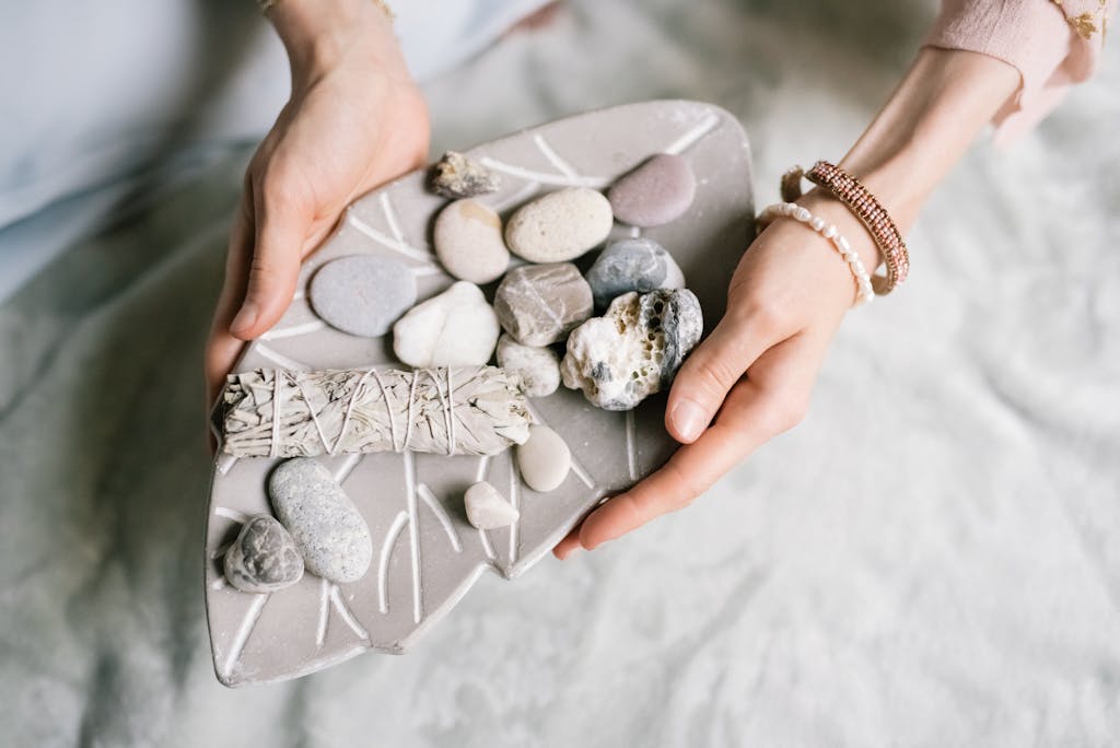 A close-up of hands holding a tray with sage and stones, ideal for meditation and relaxation.