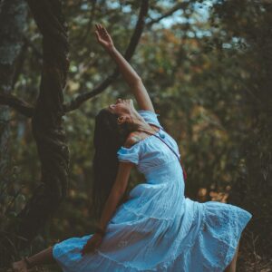 A woman in a blue dress performs a yoga pose amidst nature's tranquility.
